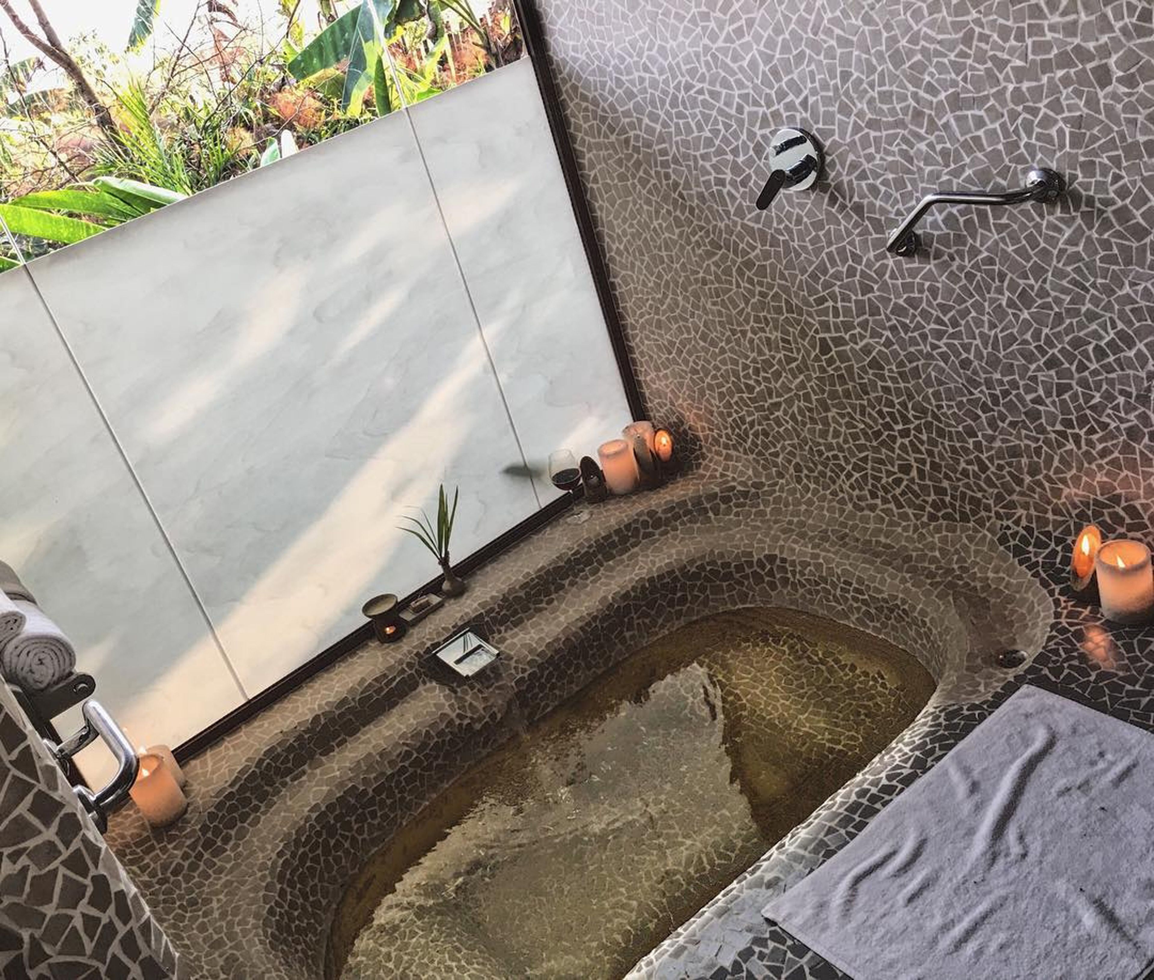 A bathroom with a stone mosaic wall, a bathtub, and a small sink.
