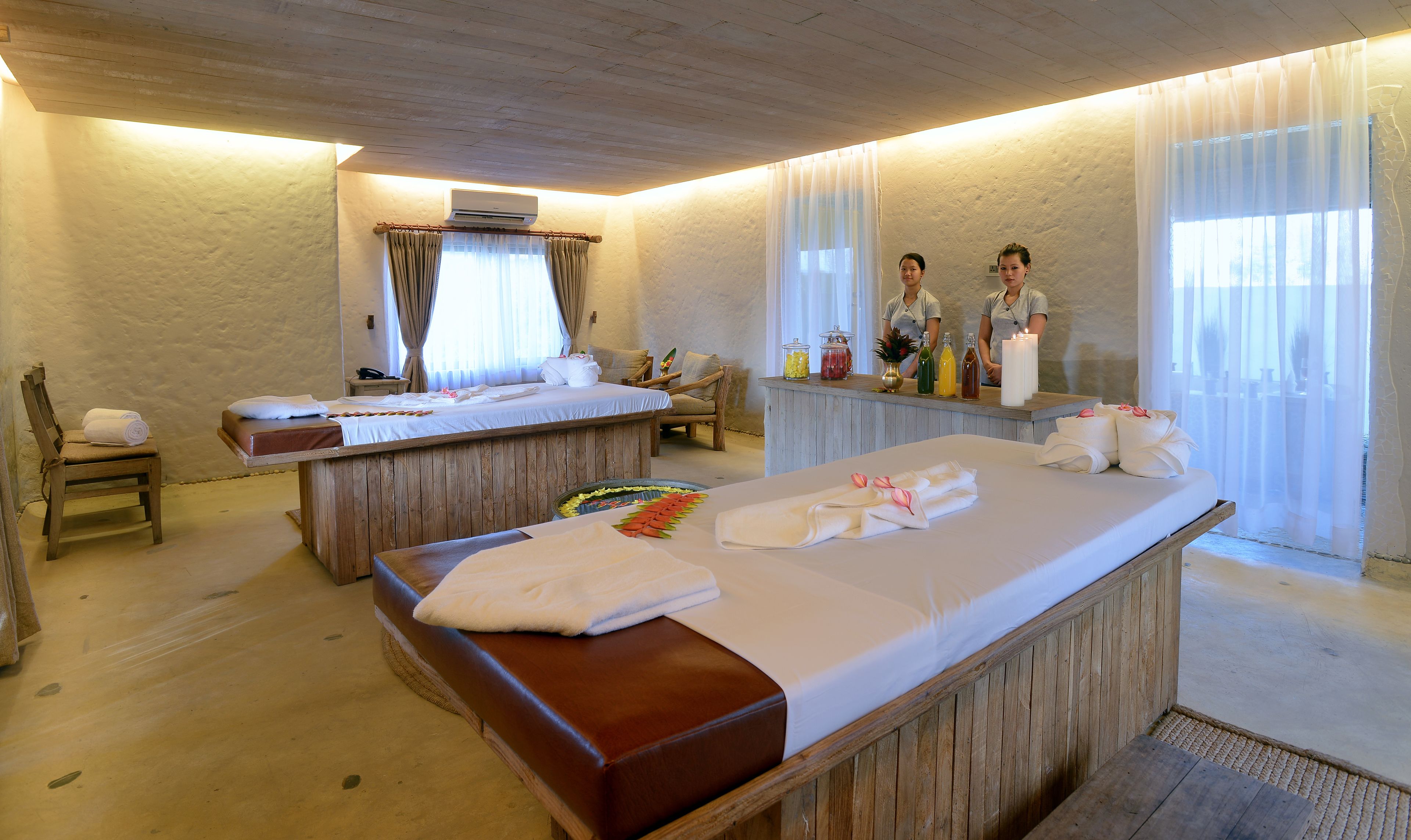 Un cuarto de spa con un banco de madera, una camilla de masaje y un mostrador de recepción con velas y refrigerios.