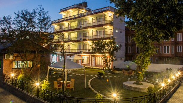 Un hotel de varios pisos con mesas al aire libre y un patio bien iluminado.