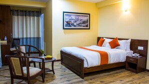 Habitación de hotel con cama, una silla, una mesita con una cesta de fruta y un cuadro en la pared.