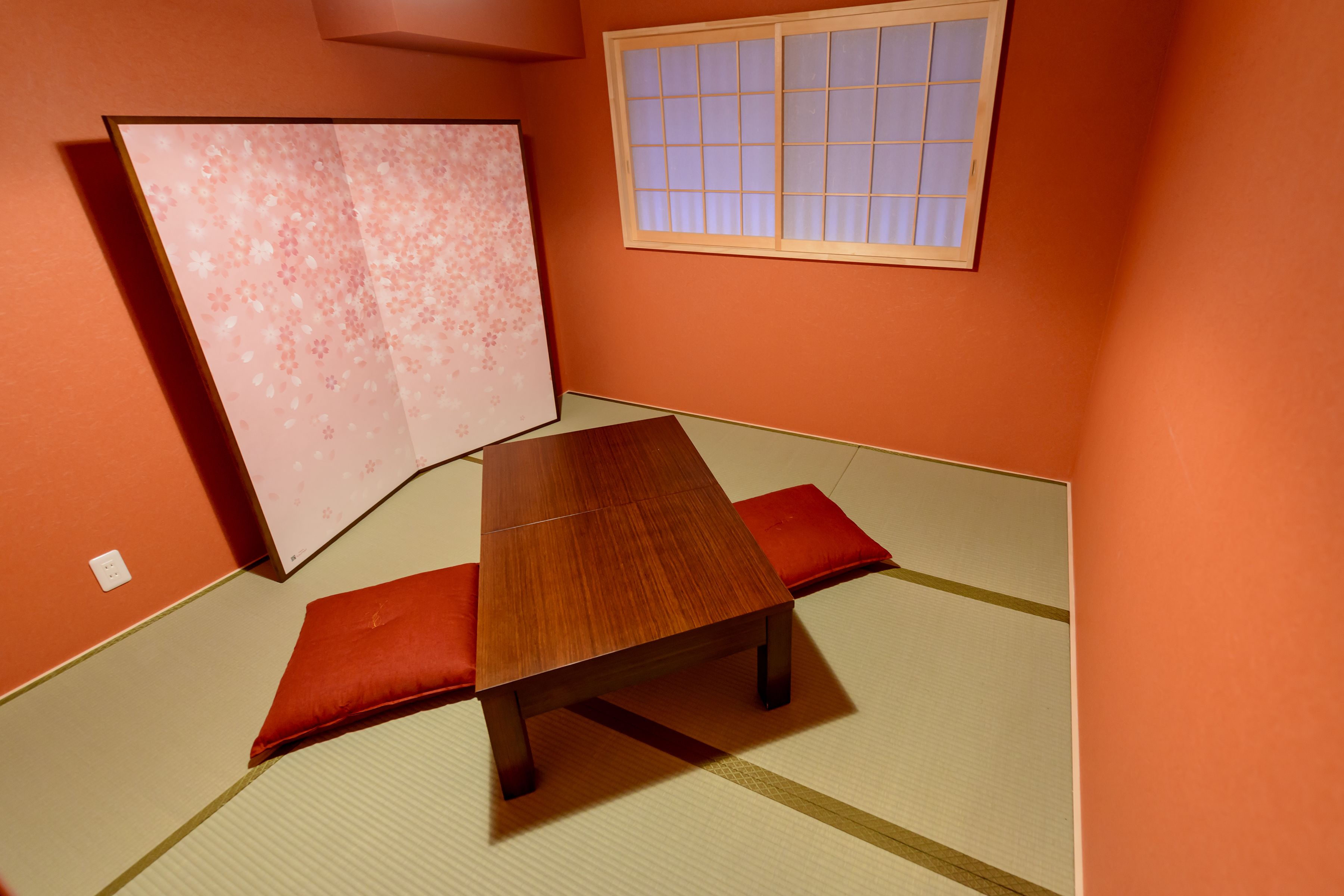 A tatami mat room with a low wooden table and red cushions.