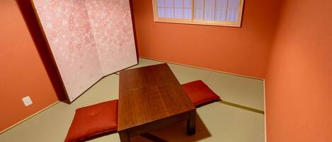 A tatami mat room with a low wooden table and red cushions.