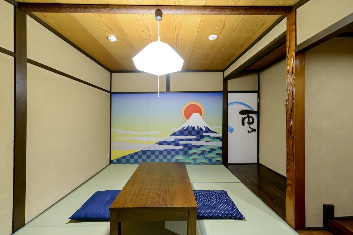 A traditional Japanese room with tatami flooring, a wooden table, and a hanging light fixture.