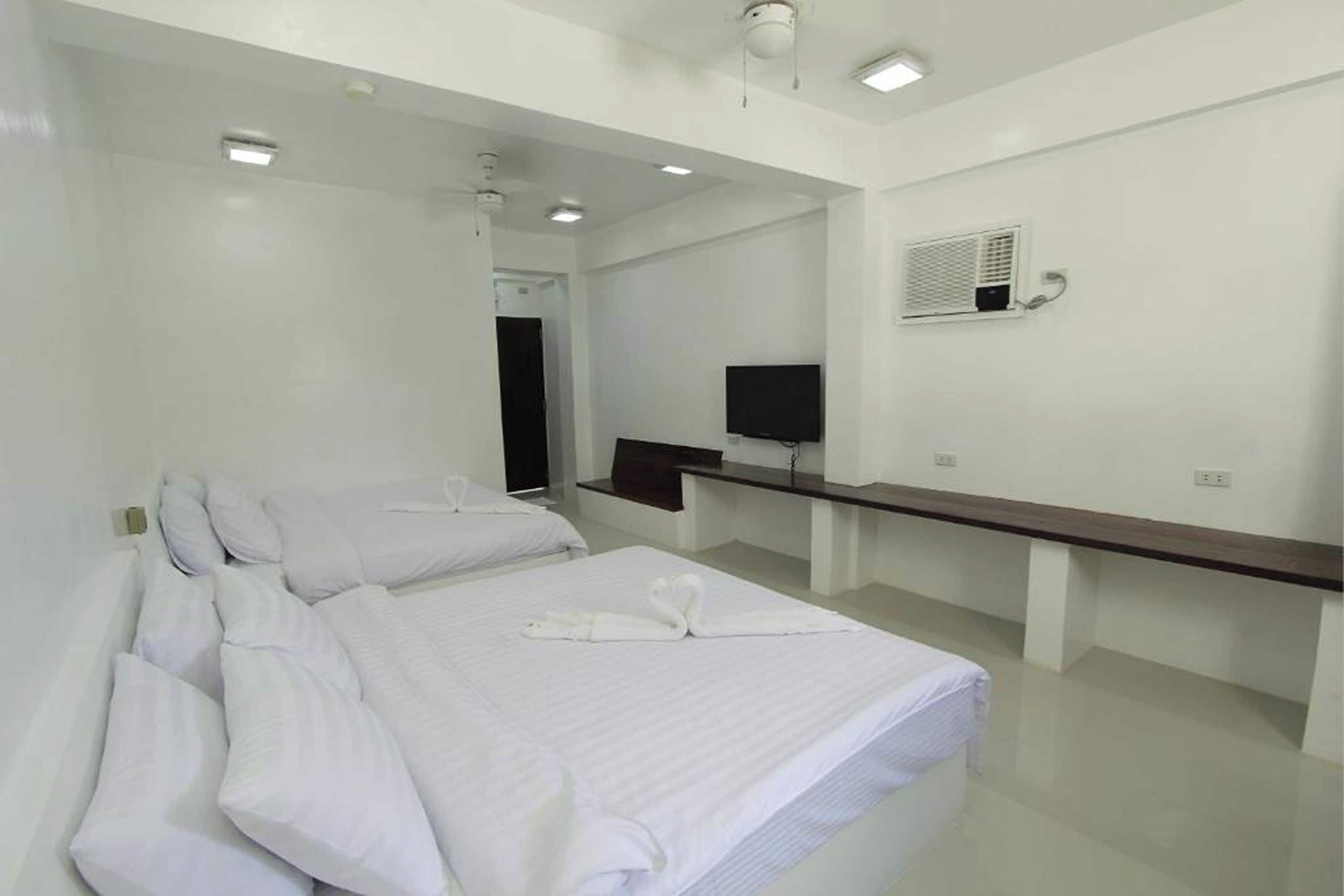 A hotel room with two beds, a flat-screen TV, a mirror, and a small desk with a chair.
