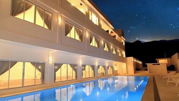 Un hotel de varios pisos con piscina, amplias ventanas y vistas a las montañas.