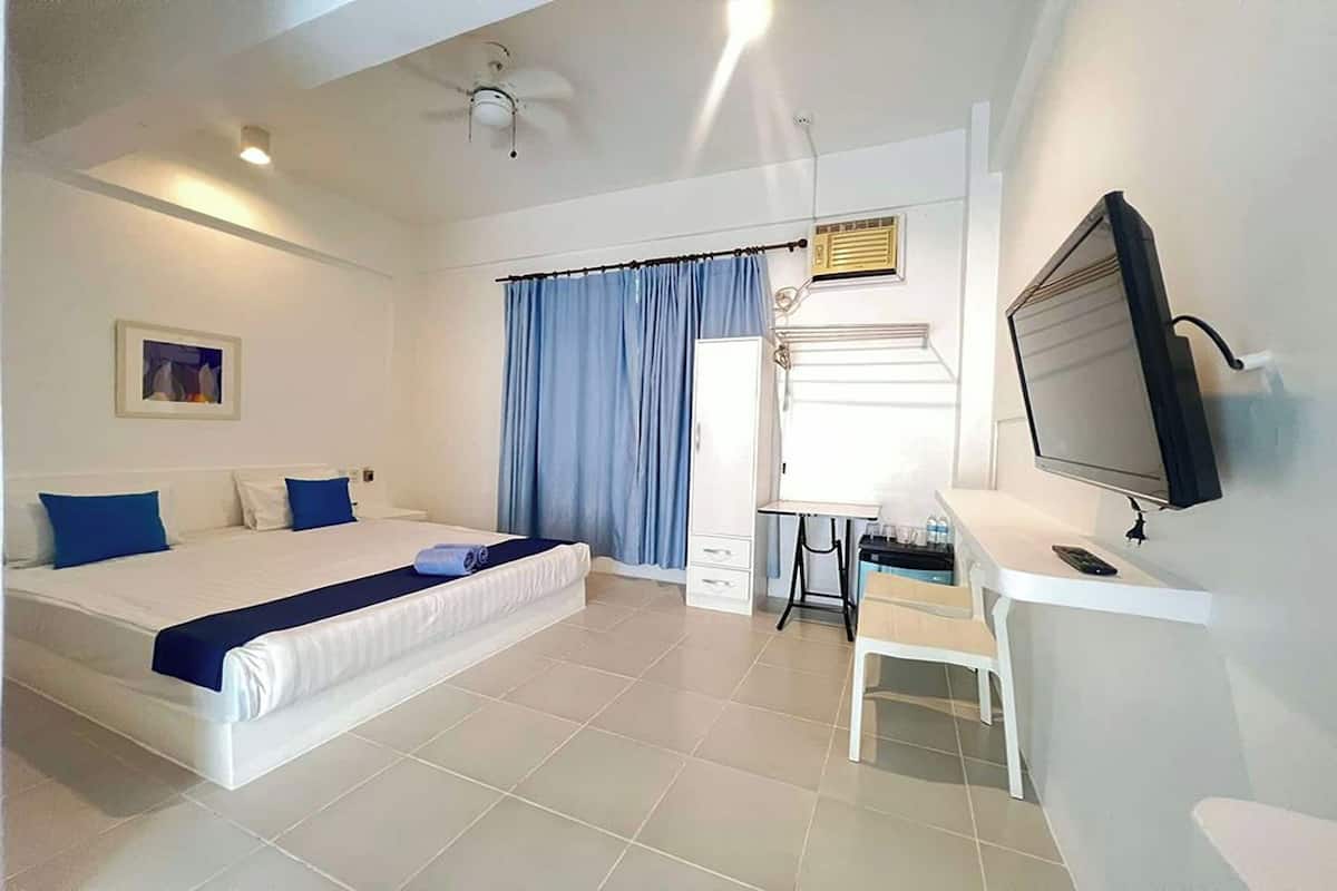 Habitación de hotel con cama, escritorio, televisor, ventana con cortinas y ventilador de techo.