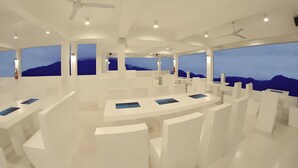 Un moderno salón de conferencias con mobiliario blanco, ventanas amplias con vistas panorámicas y ventiladores de techo.