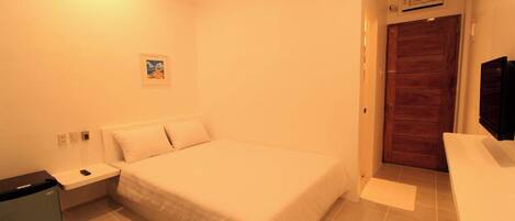 Un dormitorio con cama, mesita de noche, una pequeña mesa, un calentador en la pared y una puerta.