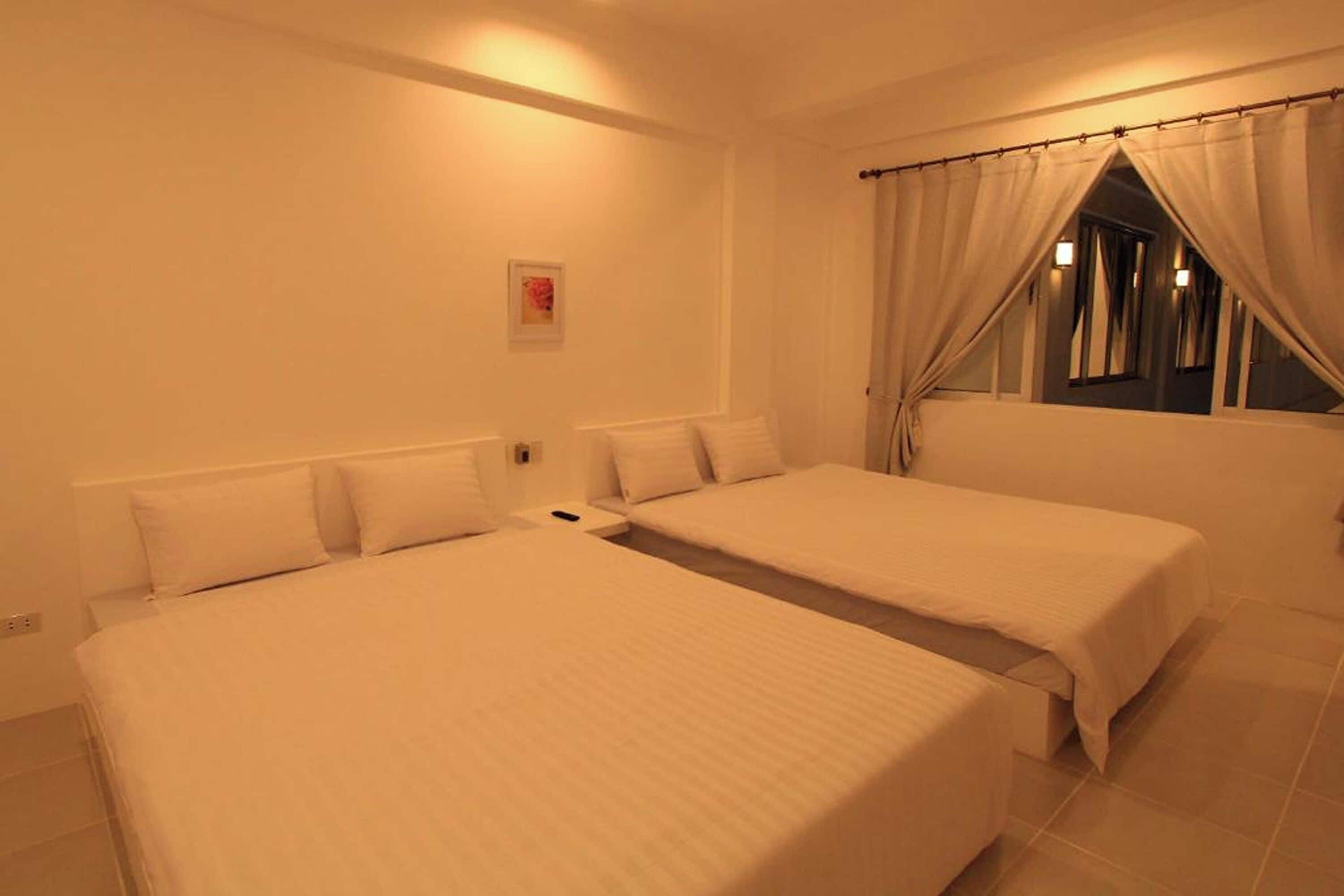 Una habitación de hotel con dos camas, una ventana con cortinas y un cuadro pequeño en la pared.