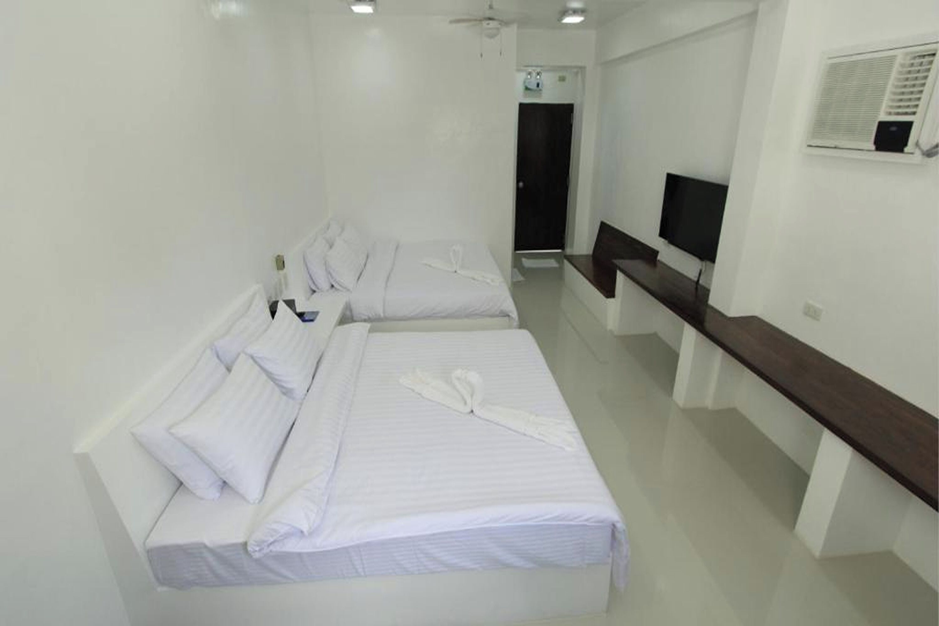 A hotel room with two beds, a flat-screen TV, and a wooden bench.