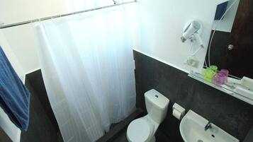 Un baño con inodoro blanco, lavamanos, cortina de ducha y secador de pelo en la pared.