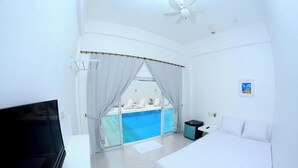 Habitación de hotel con cama, televisión, escritorio pequeño, ventana con cortinas y vista a una piscina.