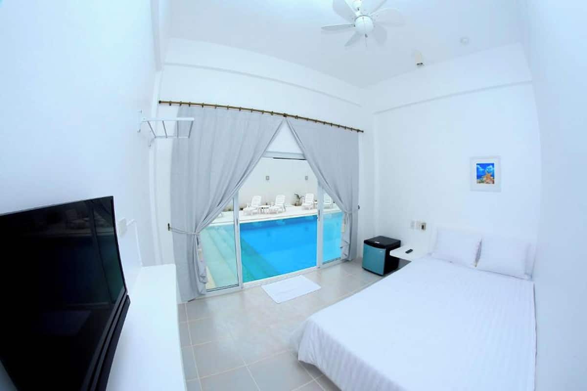 Habitación de hotel con cama, televisión, escritorio pequeño, ventana con cortinas y vista a una piscina.