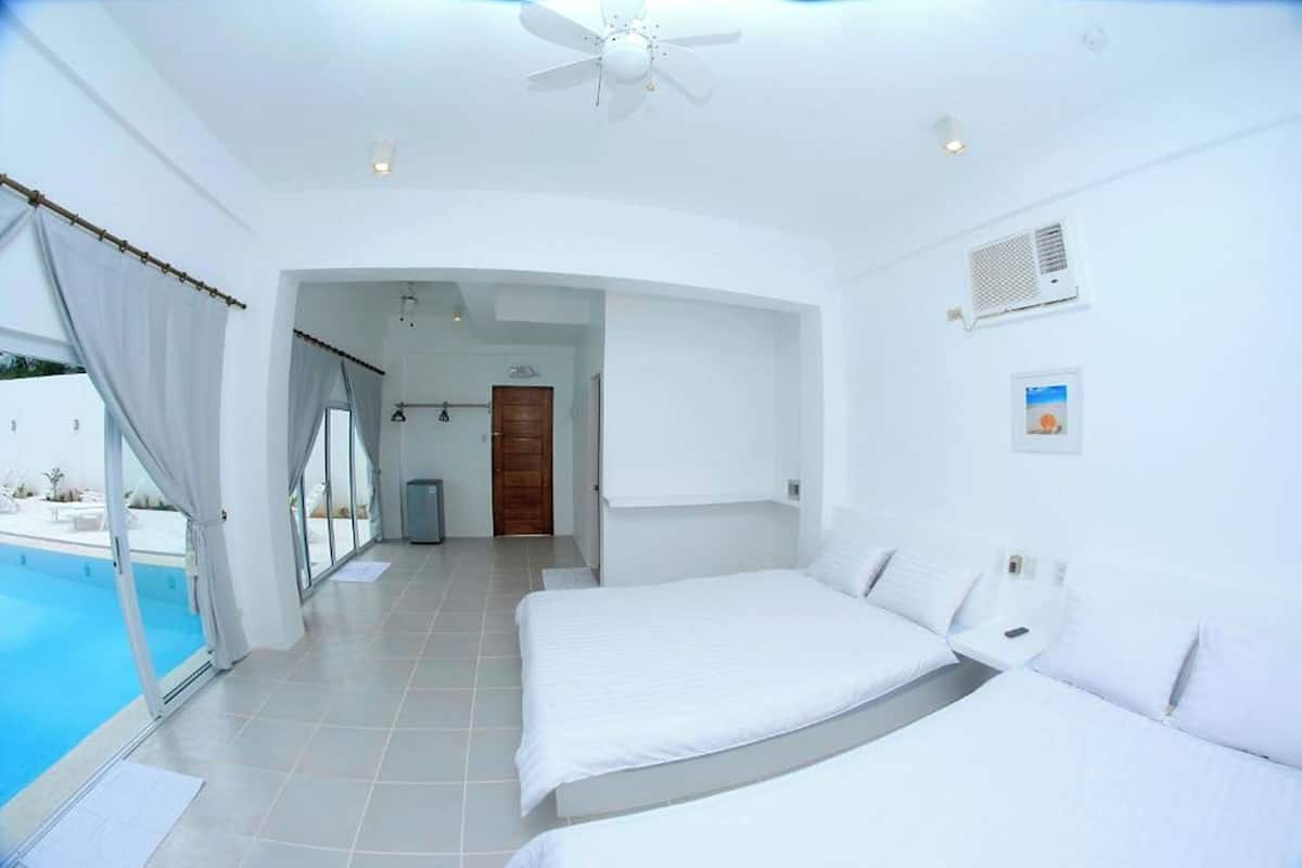 Habitación de hotel con dos camas, ventilador de techo, vista a una piscina y puerta que da a un baño.
