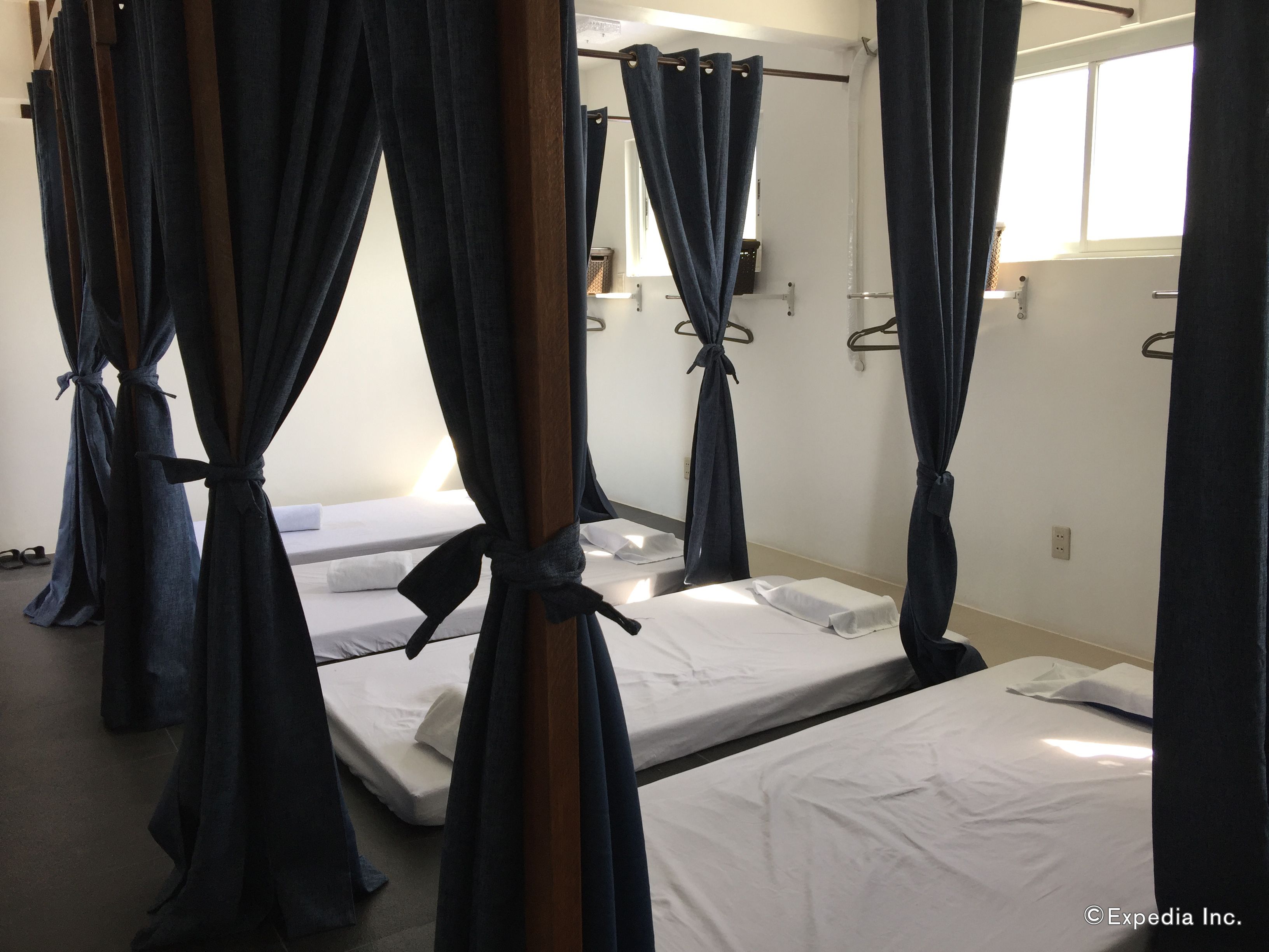A room with four beds, each with white linens and dark curtains tied at the corners.