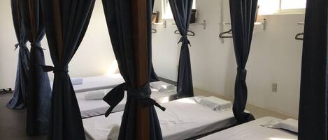 A room with four beds, each with white linens and dark curtains tied at the corners.