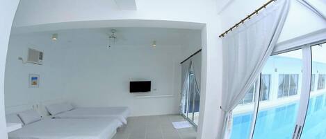 A modern hotel room with a large bed, a TV, and a balcony with a pool view.