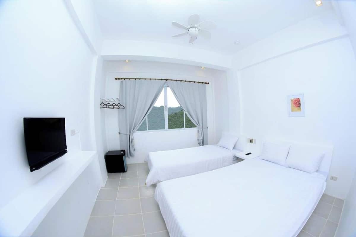 Habitación de hotel con dos camas, televisor, ventilador de techo y ventana con cortinas.