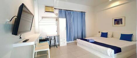 A bedroom with a bed, a desk, a chair, a television, and a ceiling fan.