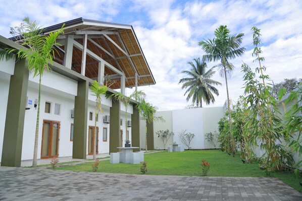 A modern building with a flat roof, large windows, and a paved courtyard with palm trees and small plants. - Hotel Cloud Nine (Negombo)