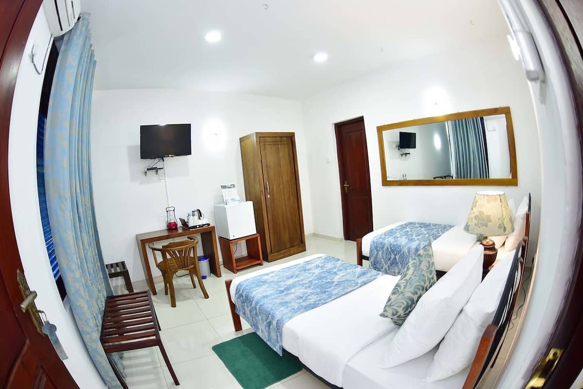 A hotel room with a bed, a desk, a chair, a television, a wardrobe, and a mirror.