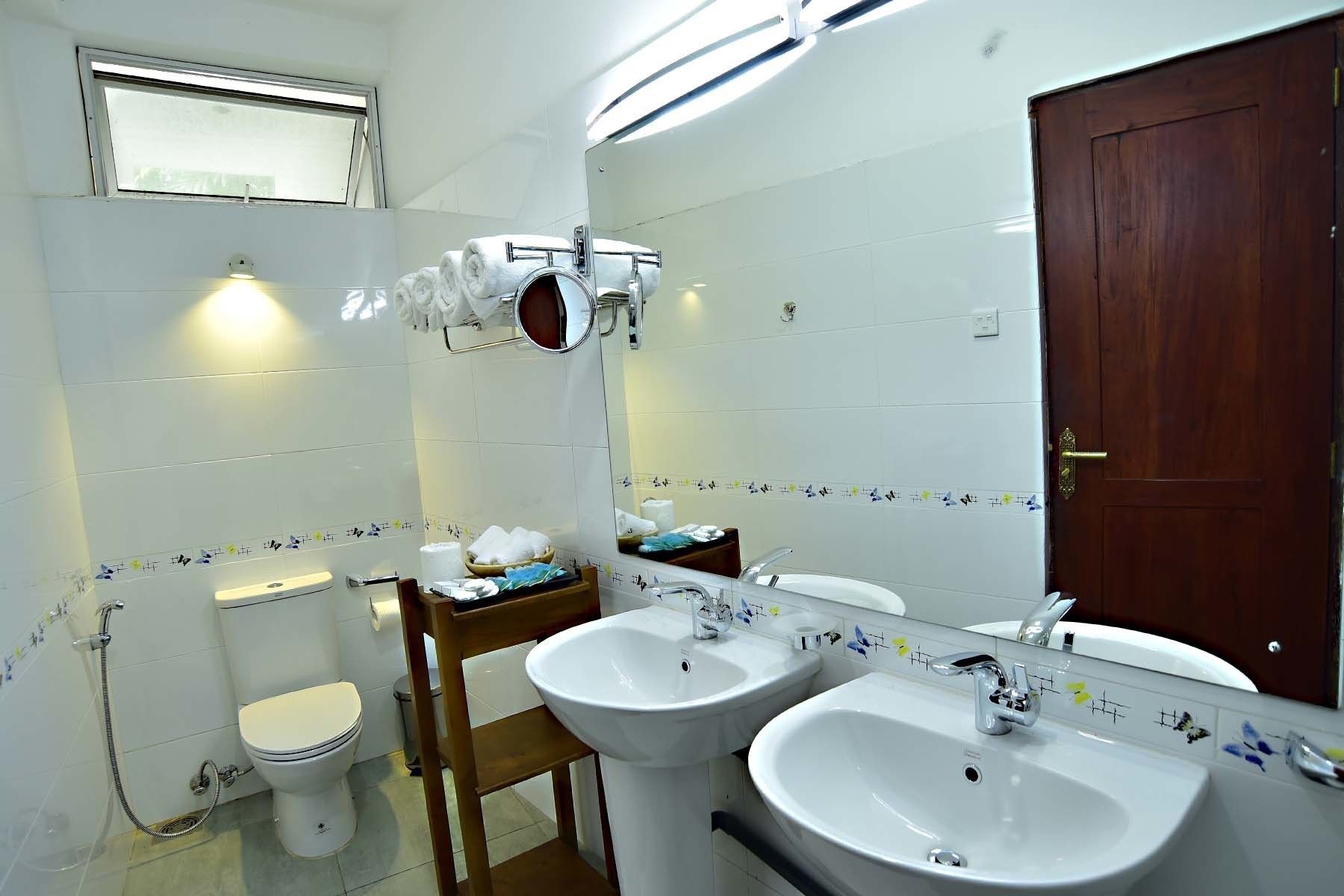 A bathroom with two sinks, a toilet, a shower, and a wooden chair.