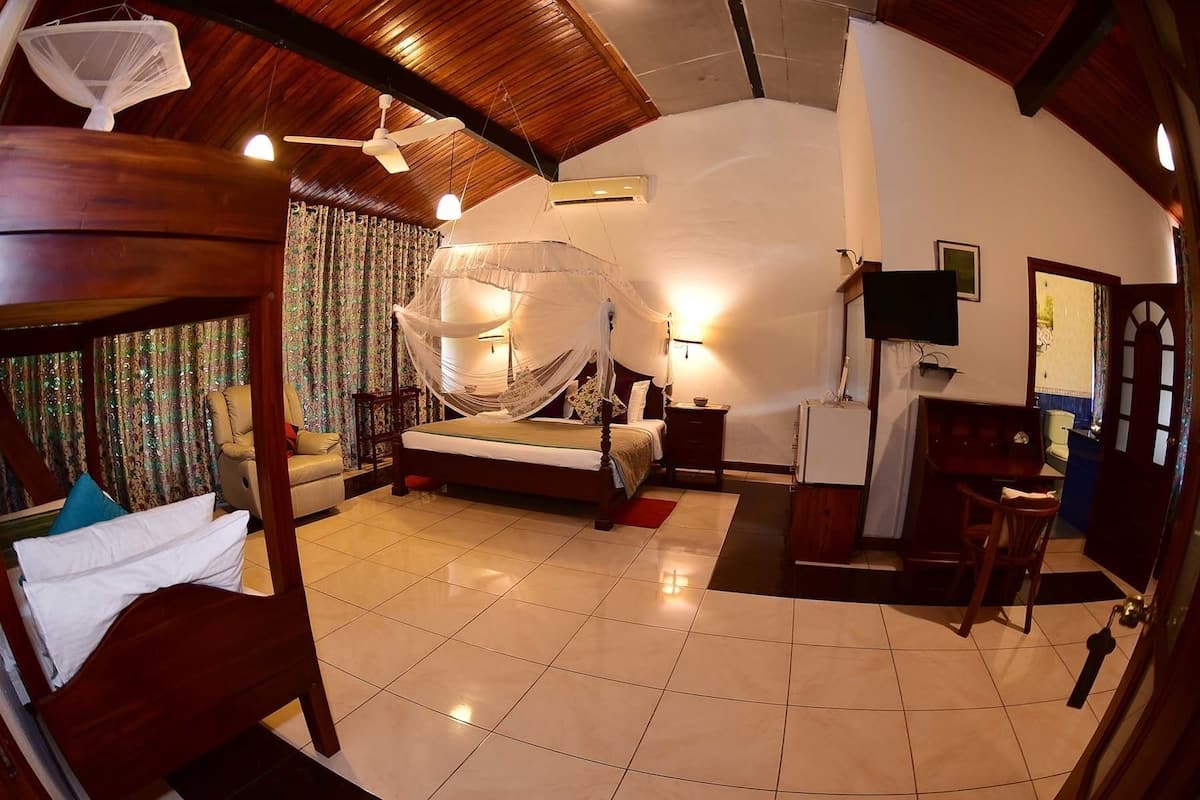 A spacious bedroom with a large bed, a ceiling fan, a TV, and a desk.