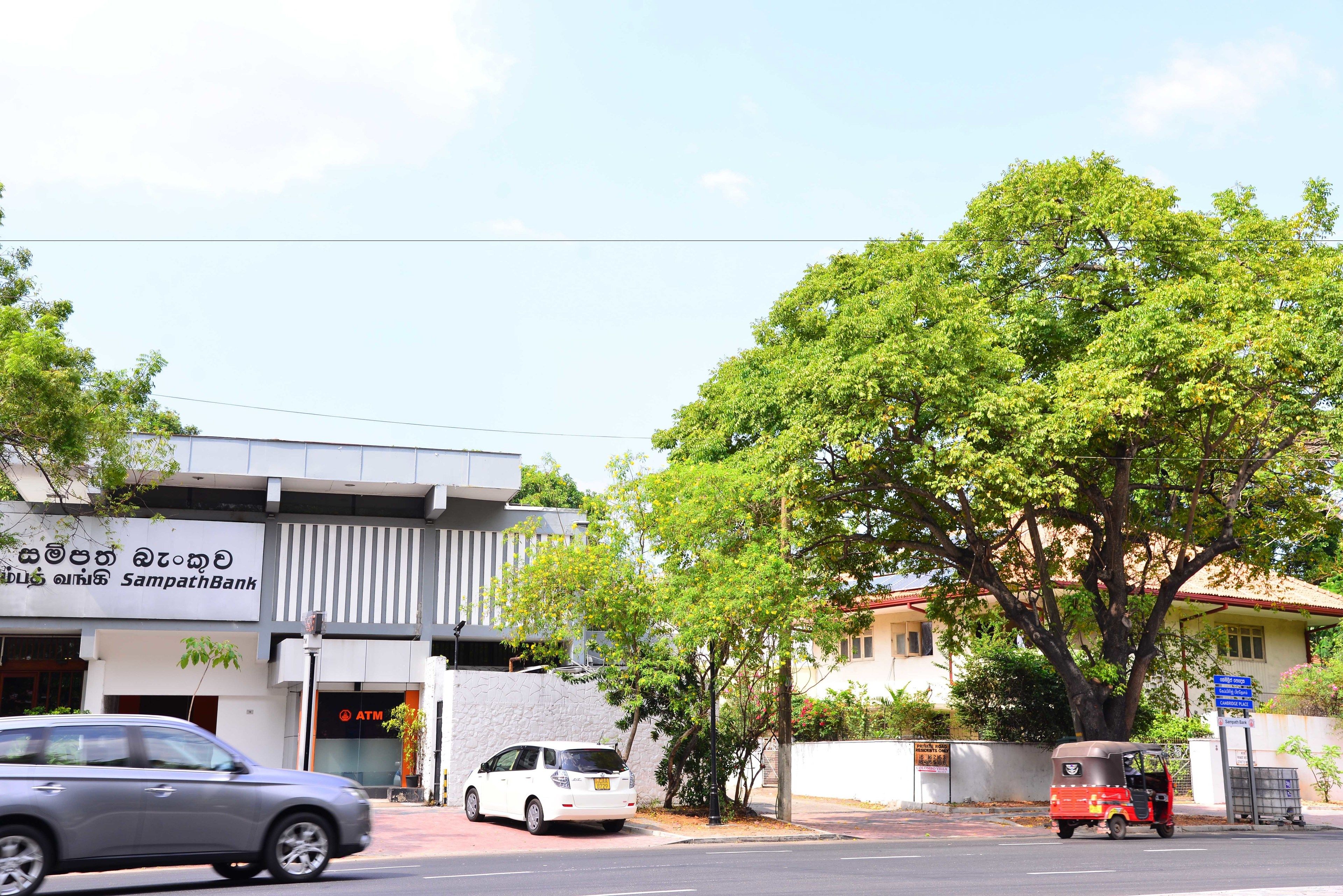 Vista de la calle con un banco, un coche estacionado y un tuk-tuk.