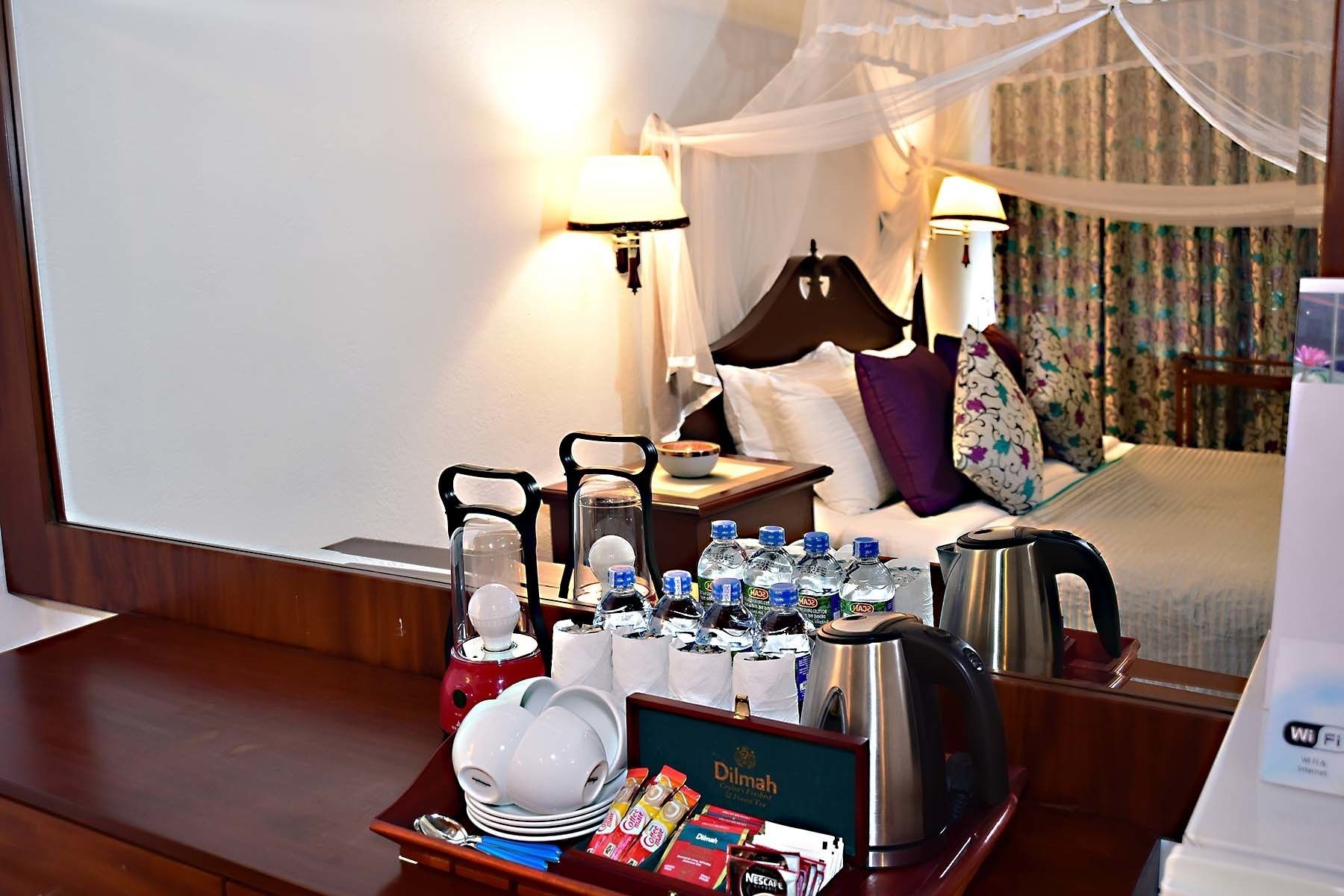 Habitación de hotel con una bandeja de desayuno ordenada, una cama con dosel y una mesita de noche con lámpara.