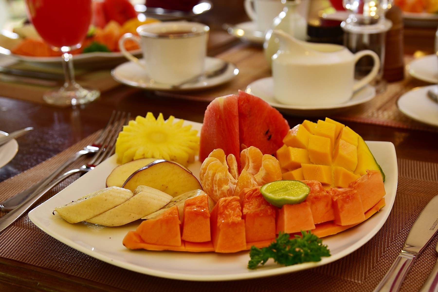 A plate of assorted fruits including watermelon, mango, pineapple, and papaya, served on a white plate with a green garnish.