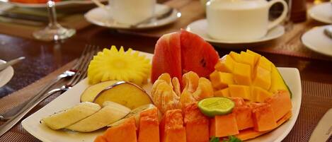A plate of assorted fruits including watermelon, mango, pineapple, and papaya, served on a white plate with a green garnish.