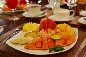 Ein Teller mit einer Auswahl an Früchten, darunter Wassermelone, Mango, Ananas und Papaya, serviert auf einem weißen Teller mit grüner Dekoration.