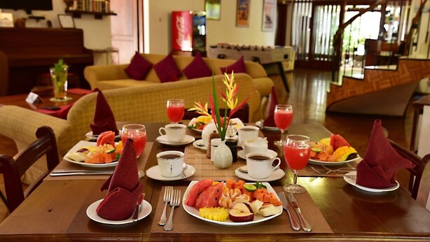 A dining table set with a variety of fruits, vegetables, and beverages, with a sofa and a staircase in the background. - Colombo Villa at Cambridge Place (Colombo)