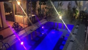 An outdoor swimming pool with blue lighting, surrounded by a patio area with chairs and tables. - Colombo Villa at Cambridge Place (Colombo)