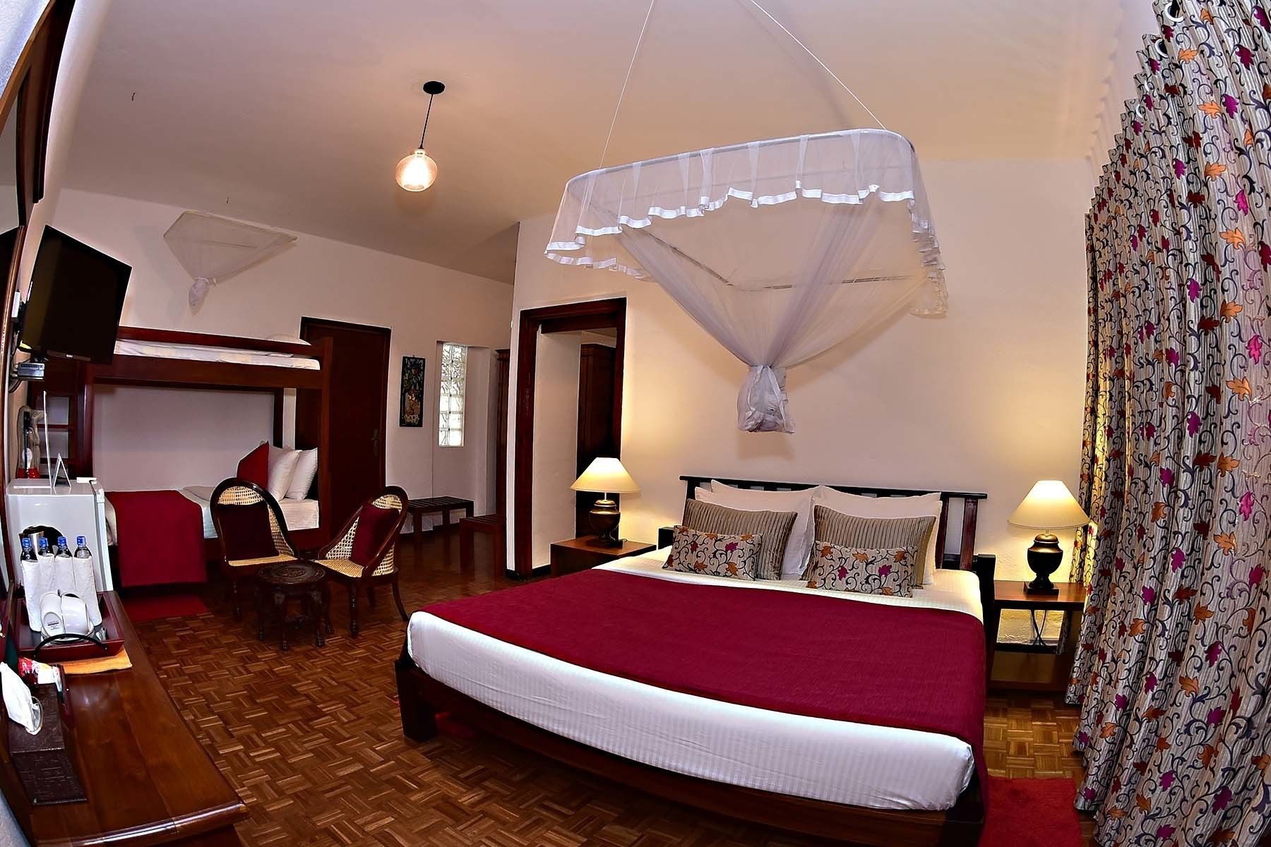 A hotel room with a large bed, a wooden floor, a TV, a desk, and a chair.