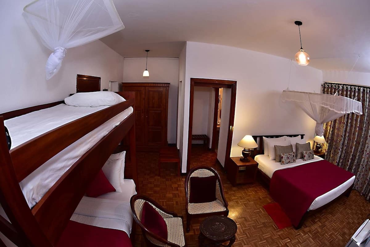 A hotel room with a bunk bed, a single bed, a chair, a small table, and a nightstand with lamps.