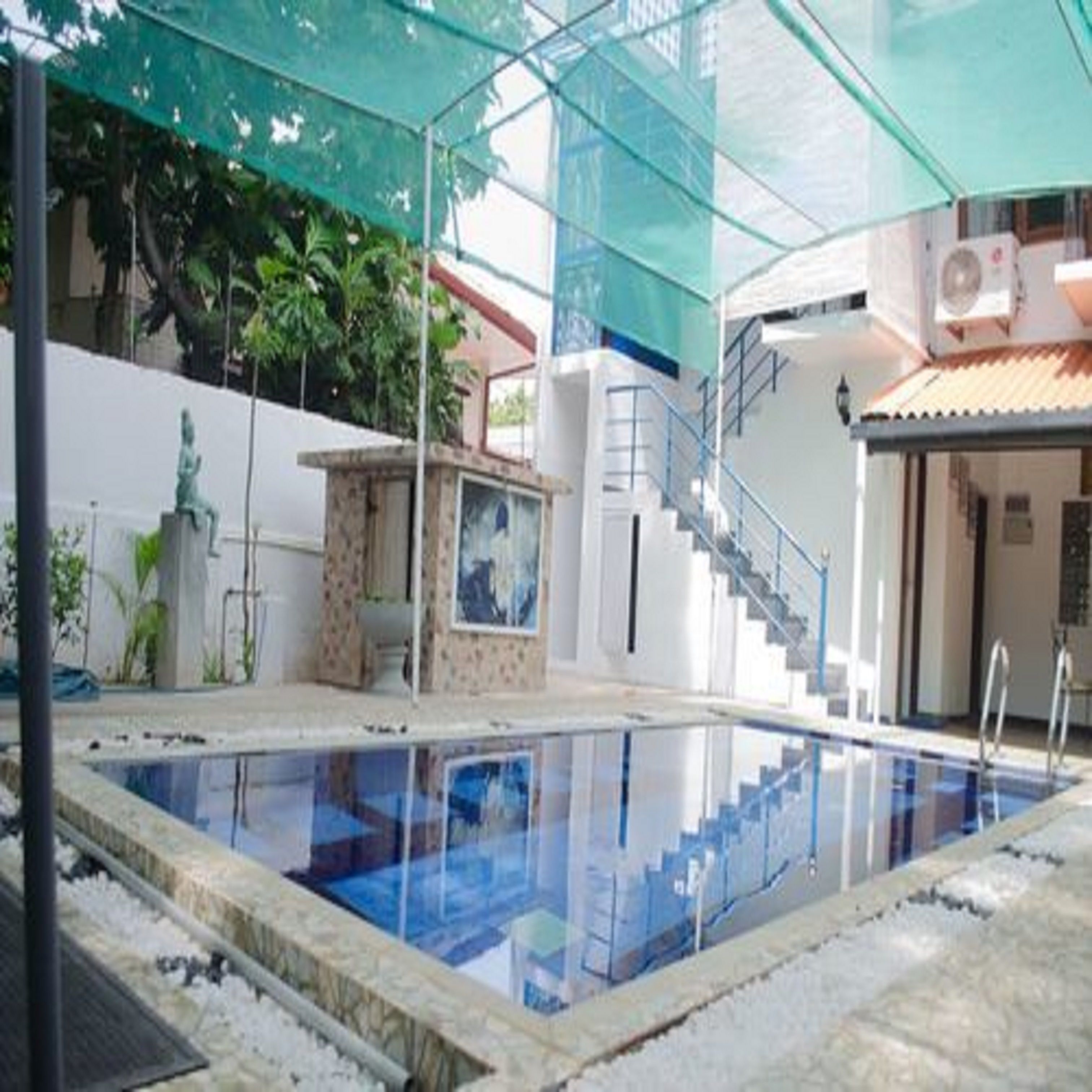 Una piscina interior con agua cristalina, rodeada por una estructura de vidrio, una escalera que lleva a un nivel superior y una estatua al fondo.
