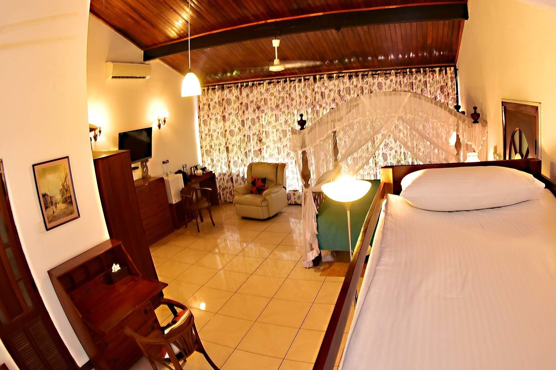 Habitación de hotel con cama, escritorio con silla, televisión y un dosel decorativo sobre la cama.