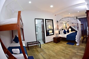 Habitación de hotel con literas, cama con dosel, mesita de noche, espejo y armario.