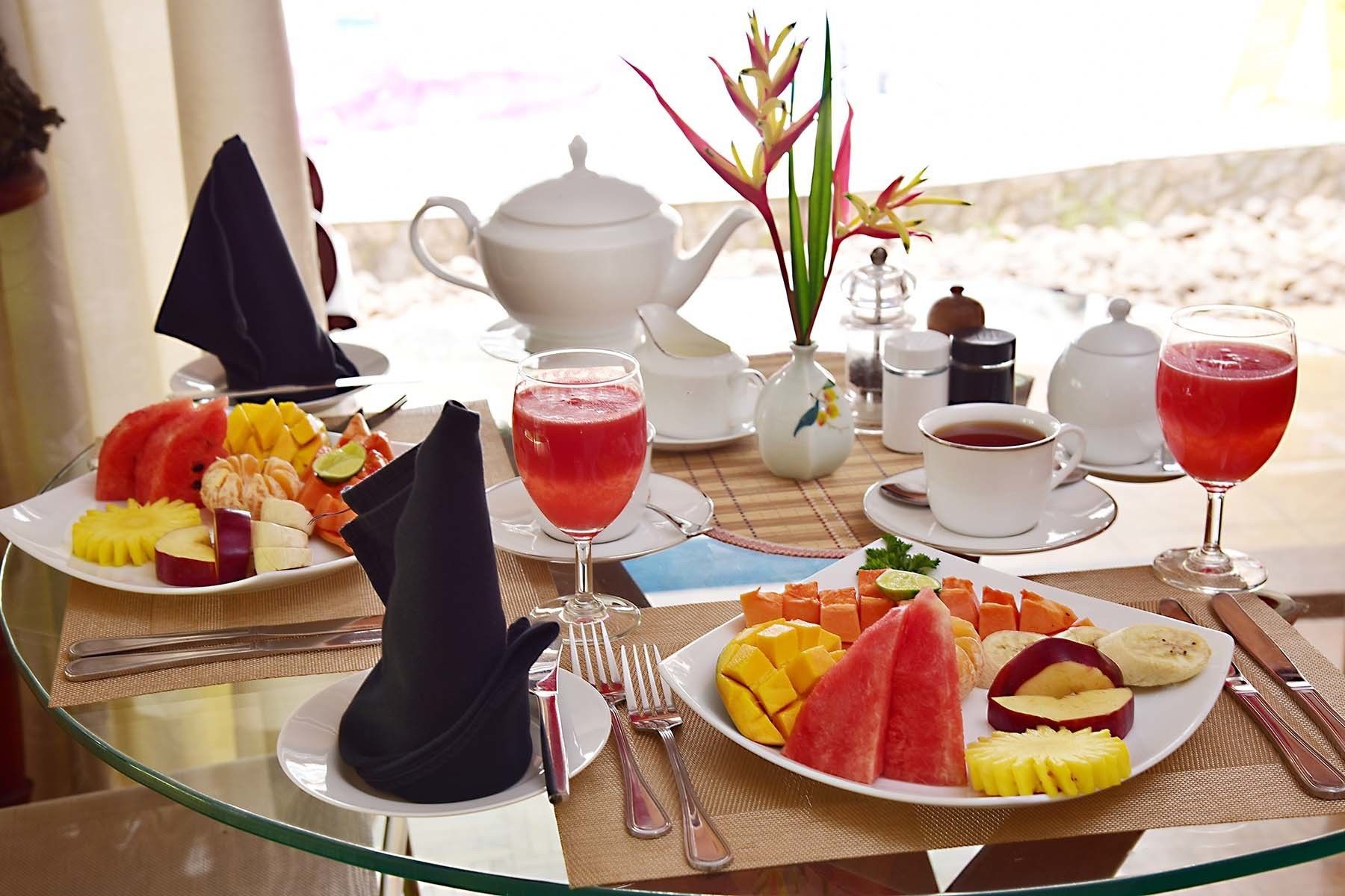 A breakfast setting with plates of fruit, a teapot, cups, and a glass of red drink.