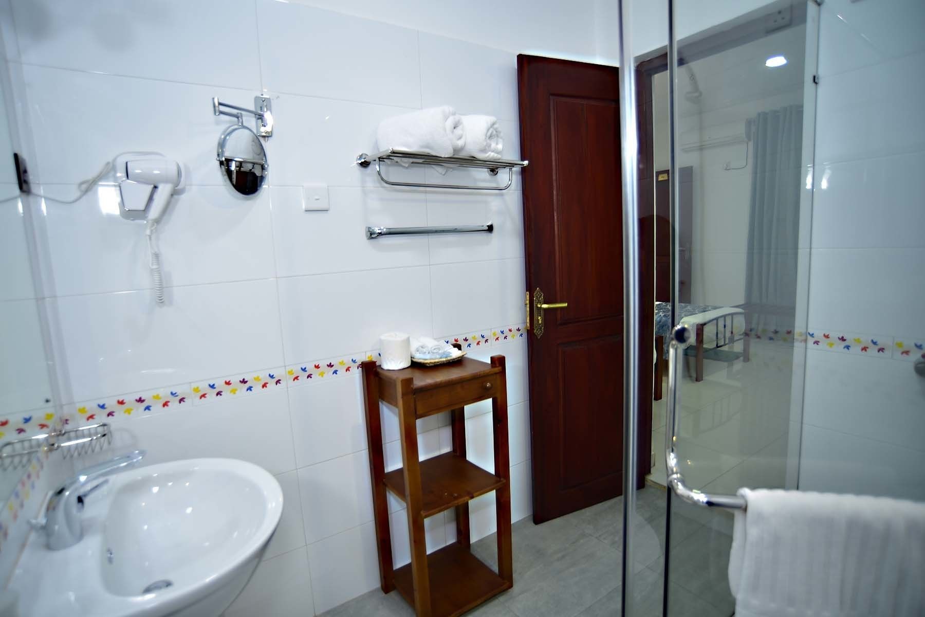 A bathroom with a sink, mirror, towel rack, and a wooden shelf.
