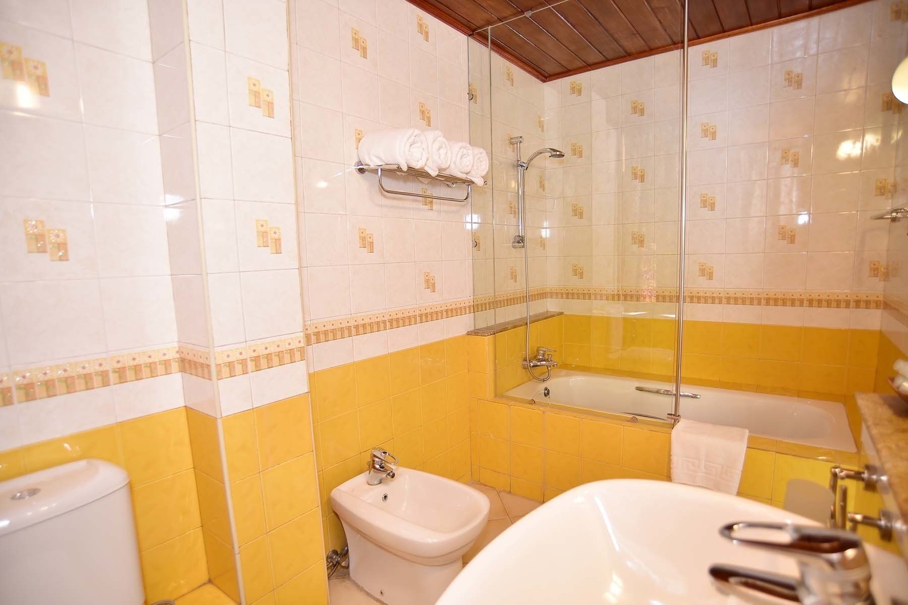 Un baño con baldosas amarillas y blancas, una bañera, un lavamanos y un inodoro.