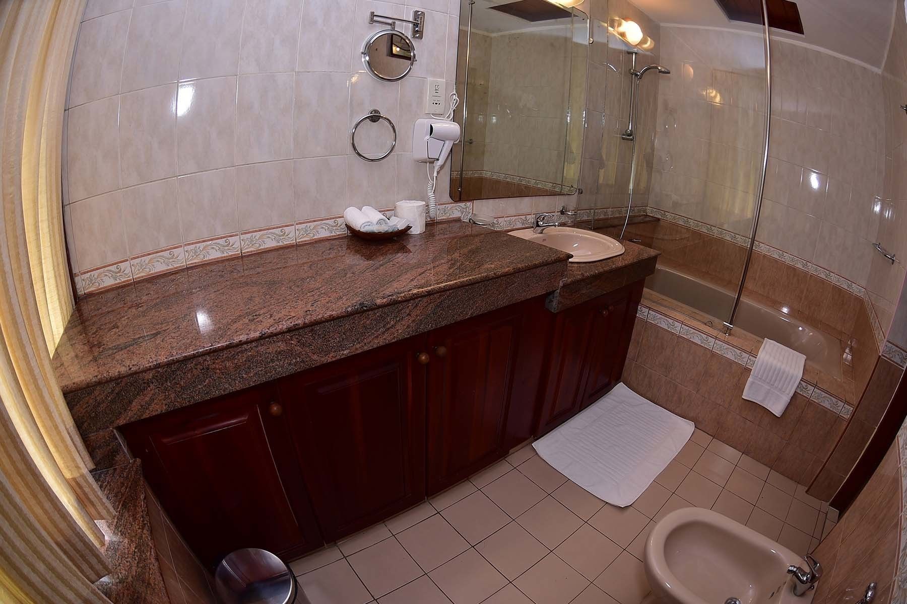 A bathroom with a marble countertop, a sink, a bidet, and a mirror.