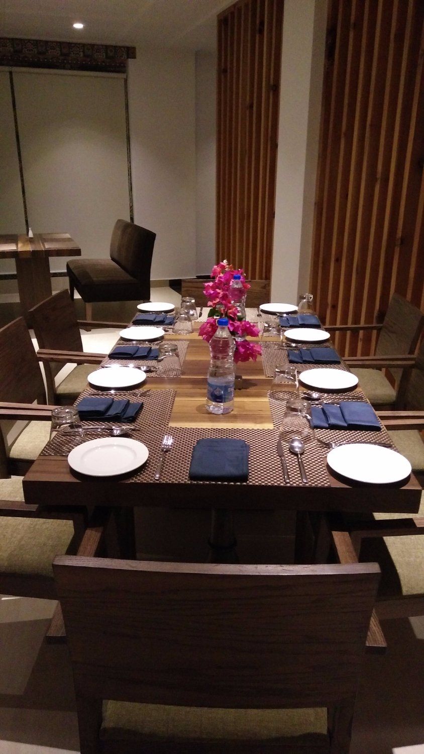A dining table set with plates, cutlery, and napkins, surrounded by chairs.