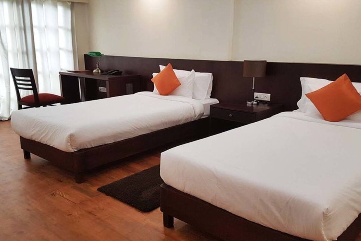 A hotel room with two single beds, a desk, a chair, and a nightstand with a lamp.