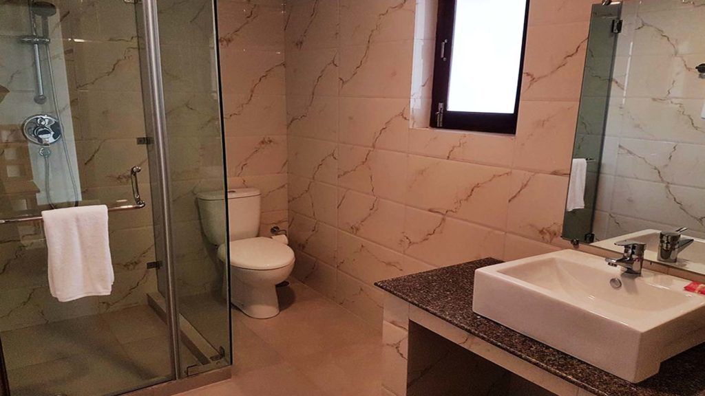 A bathroom with a glass shower enclosure, a toilet, and a sink with a marble countertop.