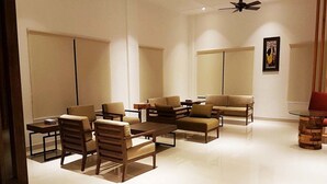 A modern, well-lit living room with a sofa, chairs, a coffee table, and a small table with a lamp. - Khuru Resort (Punakha)