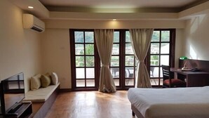 A hotel room with a bed, a desk, a TV, and a seating area by a large window with curtains. - Khuru Resort (Punakha)