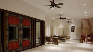 A spacious living room with a modern design, featuring a large sofa set, a dining table, and multiple ceiling fans. - Khuru Resort (Punakha)