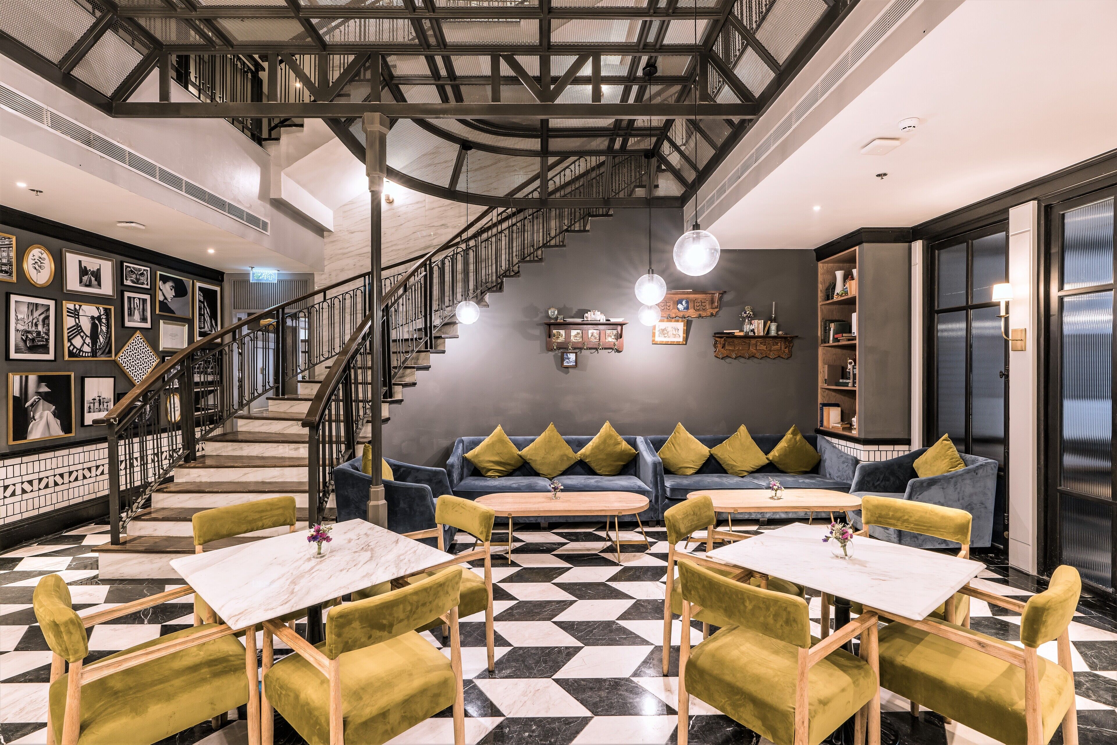 A modern interior with a checkered floor, a staircase, a sofa with cushions, and tables with chairs.